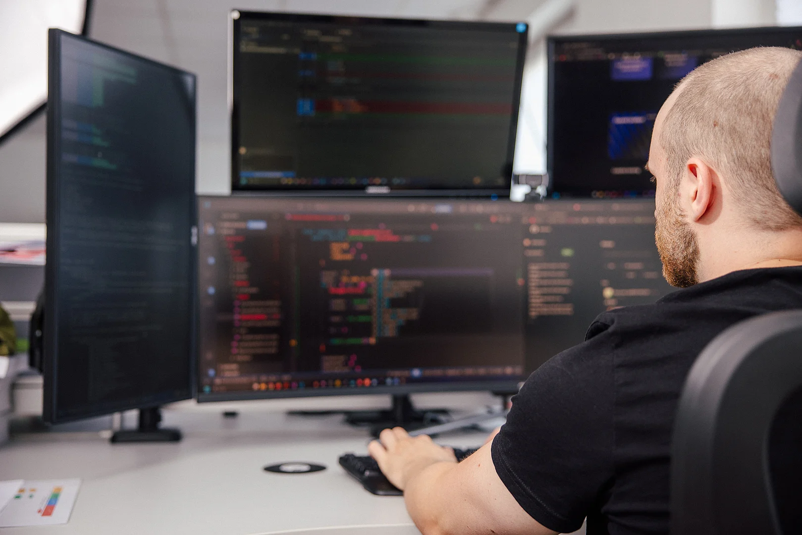 Person am Schreibtisch mit drei Bildschirmen und Code-Editor